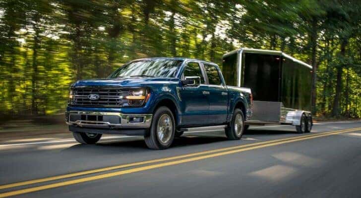 A blue 2024 Ford F-150 for sale is shown from the front at an angle while towing a trailer.