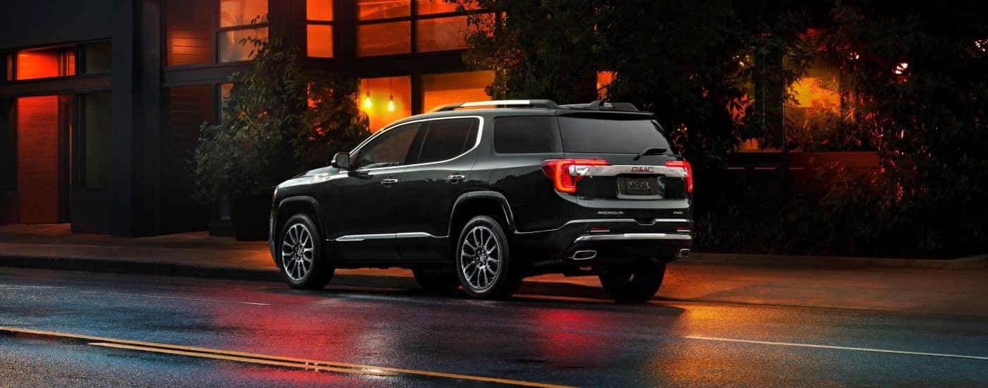 Rear view of a black 2023 GMC Acadia Denali parked on a city street in the evening.