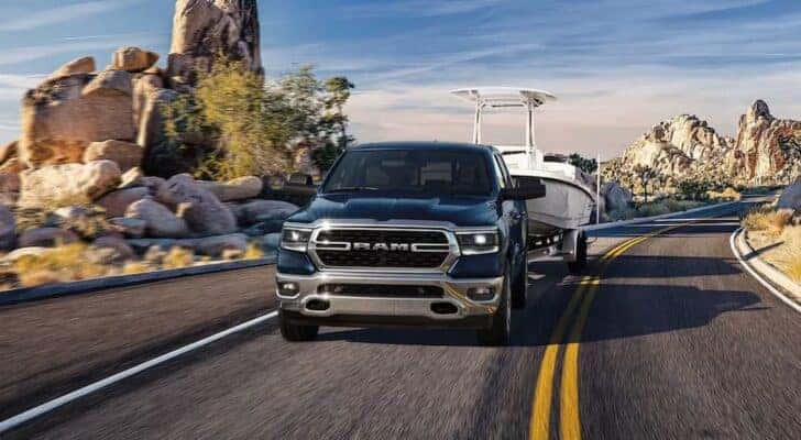 A blue 2023 Ram 1500 for sale in Cleveland is shown from the front while towing a boat.