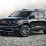 A black 2017 GMC Acadia parked on rocky terrain and angled left.