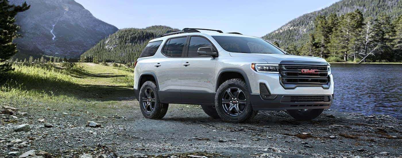 A white 2023 GMC Acadia AT4 parked off-road near a lake.