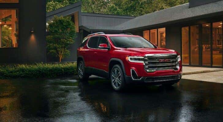 A red 2023 GMC Acadia parked in front of a modern home.