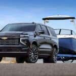 A black 2025 Chevy Suburban High Country is shown from the front at an angle while towing a boat.