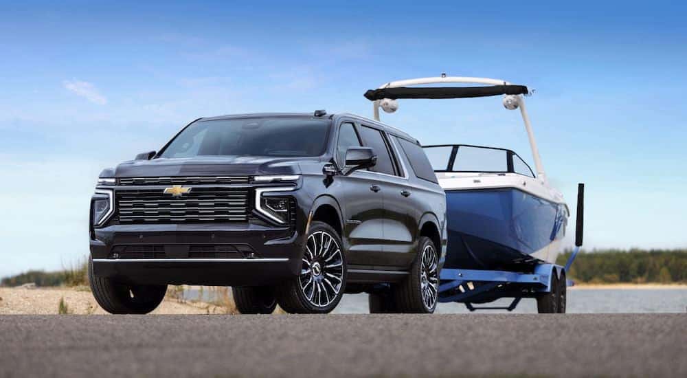 A black 2025 Chevy Suburban High Country is shown from the front at an angle while towing a boat.