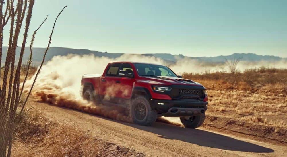 A red 2022 Ram 1500 TRX kicking up dust while off-roading on a trail.