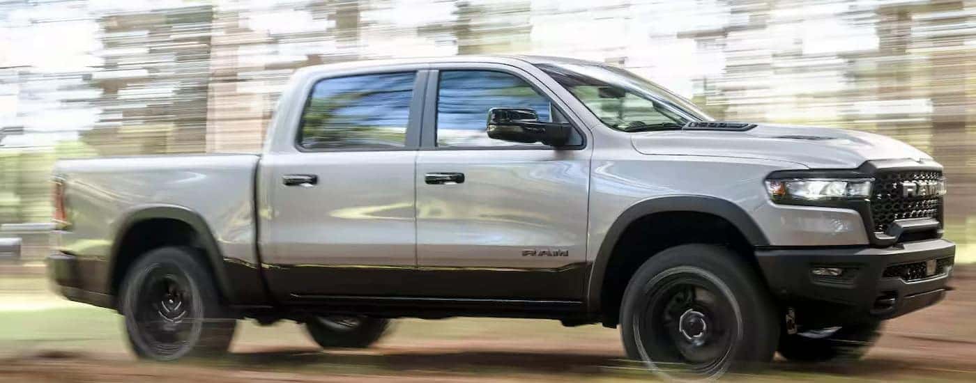Side angle view of a white 2024 Ram 1500 driving through a forest.