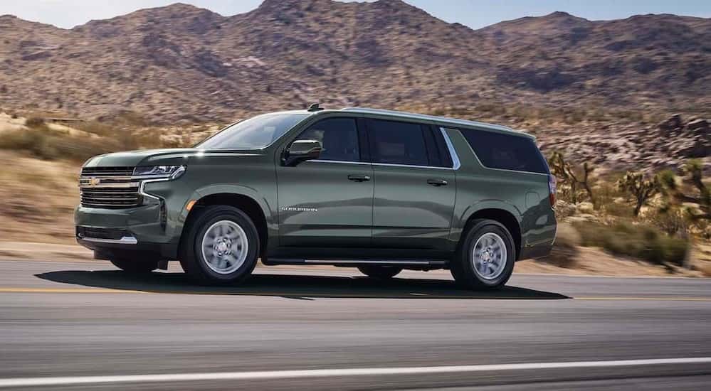 A green 2023 Chevy Suburban is shown driving on a highway after viewing a used Chevy Suburban for sale.