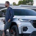 A man with a camera leaning up against a white 2023 Chevy Traverse Redline for sale in Cleveland.