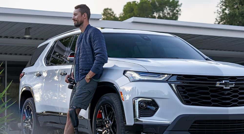 A man with a camera leaning up against a white 2023 Chevy Traverse for sale in Cleveland.