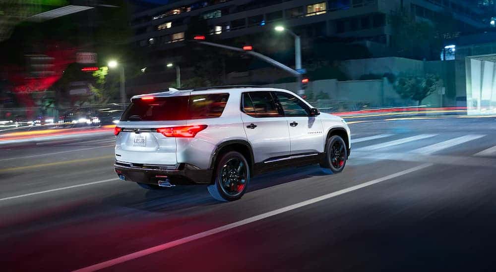 Rear view of a white 2023 Chevy Traverse Redline driving through a city at night.