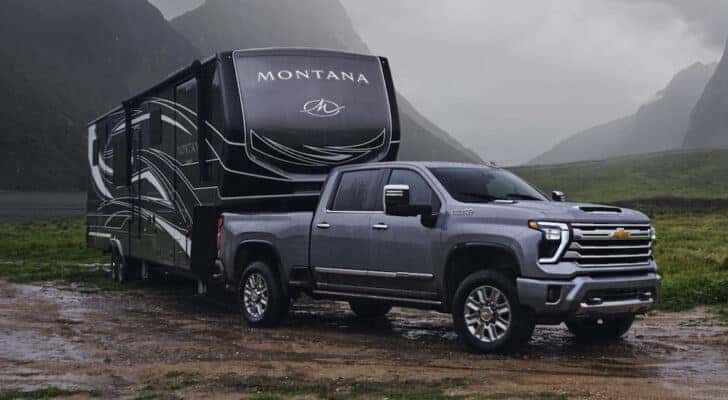 A grey 2024 Chevy Silverado 2500 towing an RV through a muddy field.