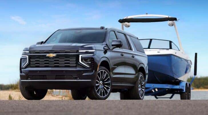 A black 2025 Chevy Suburban High Country is shown towing a boat.