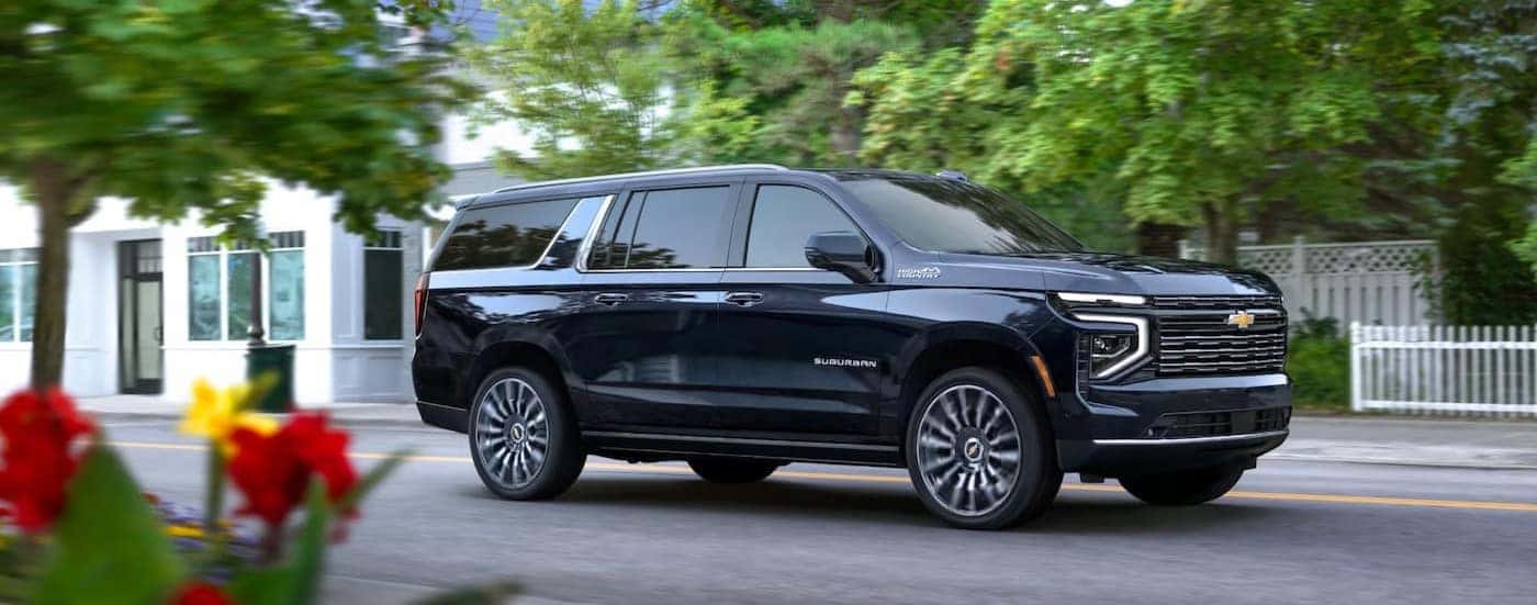 A black 2025 Chevy Suburban High Country is shown driving on a city street.