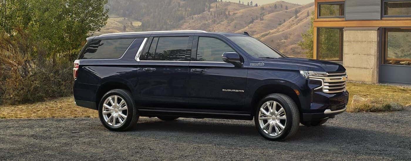 Side angle view of a dark blue 2024 Chevy Suburban High Country parked on a driveway.