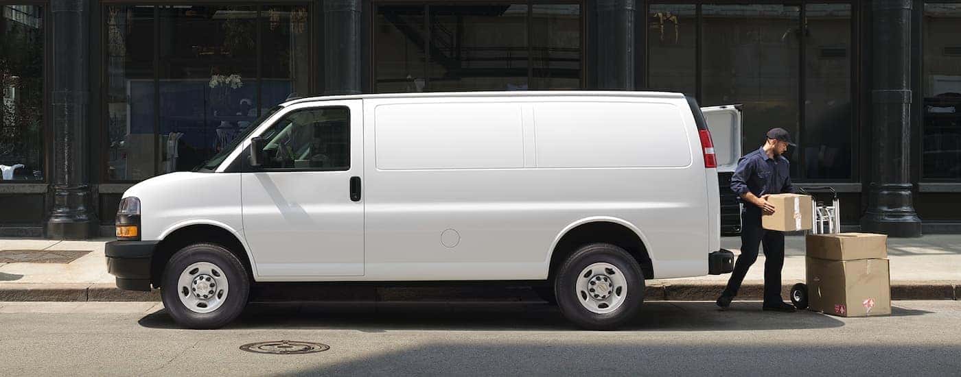Side angle view of a man unloading boxes from the back of a white 2025 Chevy Express 2500 Cargo Van for sale.