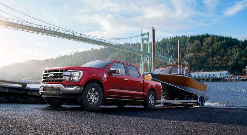 A red 2023 Ford F-150 towing a boat out of a river.