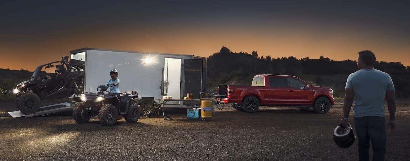 A red 2023 Ford F-150 for sale in Fort Worth is shown unloading a trailer of ATVs.