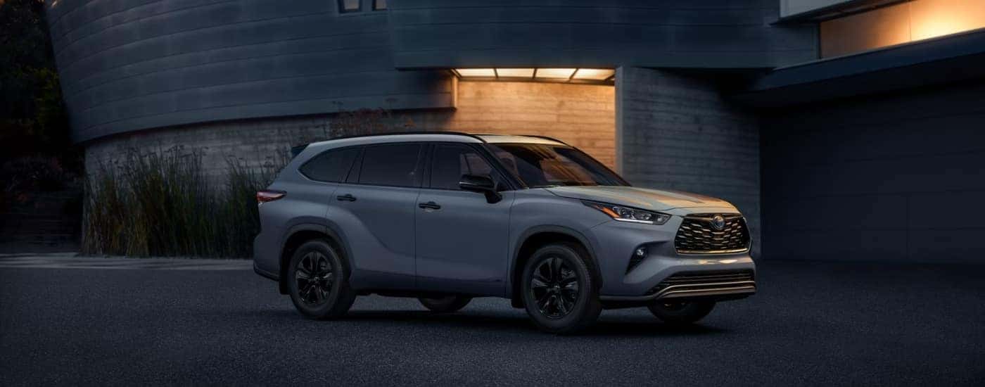 A silver Toyota Highlander for sale is parked in front of a modern house at night.