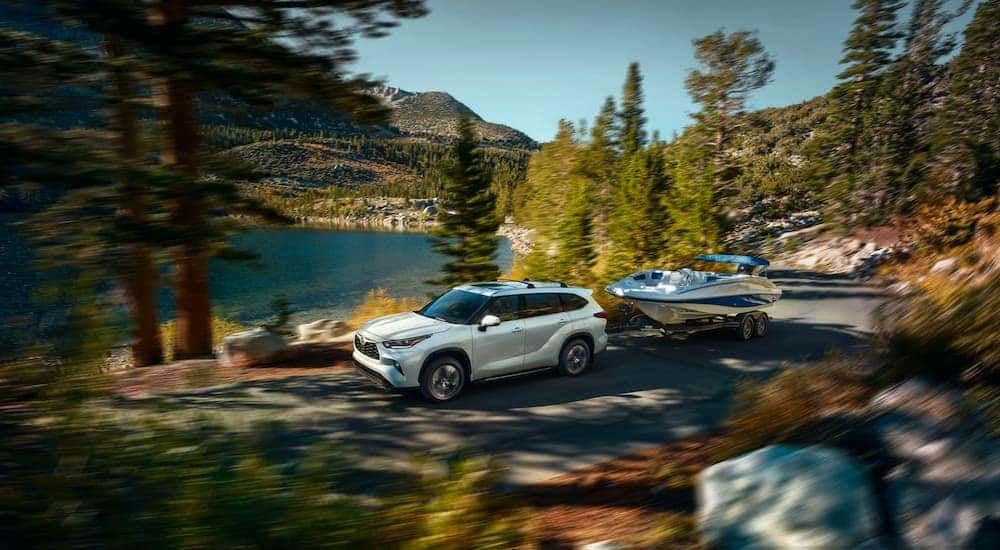 White 2023 Toyota Highlander XLE towing a boat down a forest road.