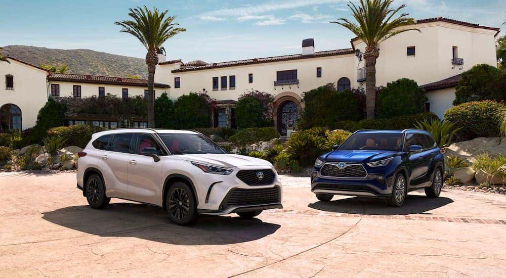 White and a blue 2023 Toyota Highlander parked beside each other outside a building.
