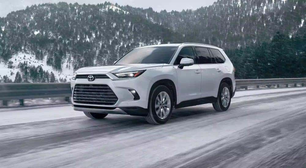 White 2024 Toyota Grand Highlander driving on a snowy road.