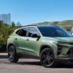 A green 2024 Chevy Trax for sale is parked near three people.