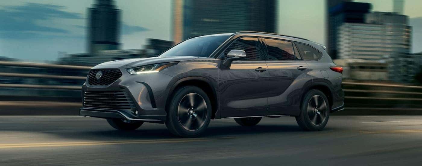 A grey 2022 Toyota Highlander for sale driving past city buildings.