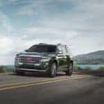 A green 2023 GMC Acadia Denali driving on a highway.