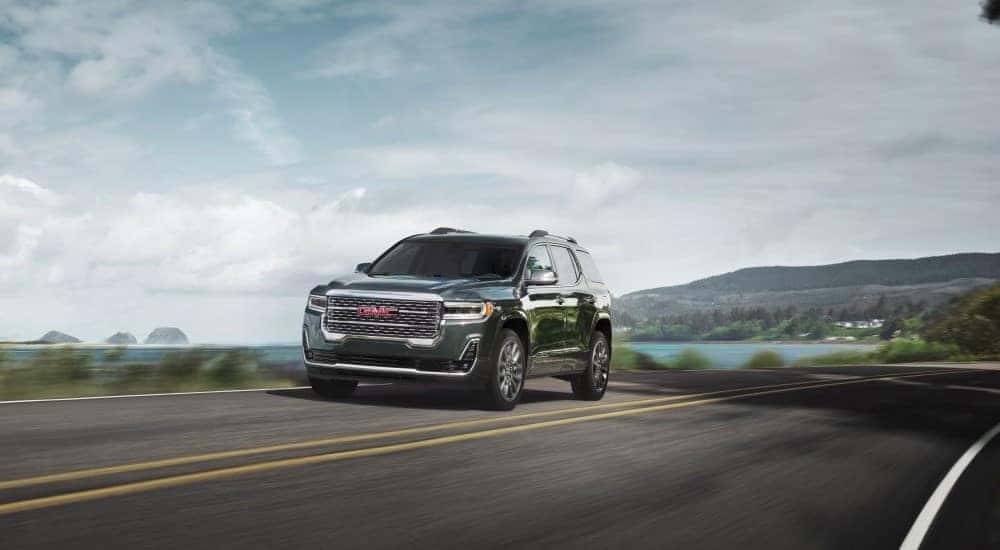A green 2023 GMC Acadia Denali driving on a highway.