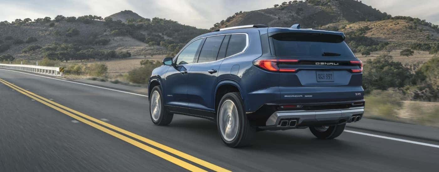 A blue 2025 GMC Acadia Denali driving down a highway