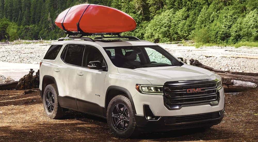 White 2022 GMC Acadia driving off-road with a kayak on the roof.
