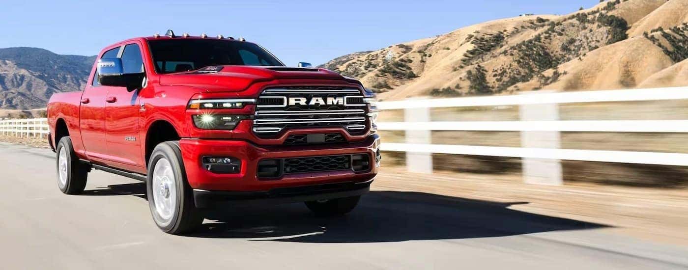 A red 2025 Ram 2500 driving near a white fence.