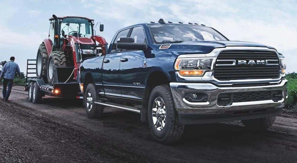 Blue 2021 Ram 2500 towing a tractor off-road.
