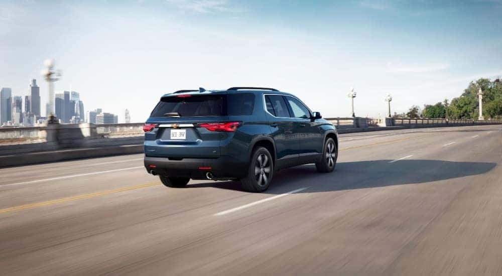 Rear of a blue 2023 Chevy Traverse driving down a road.