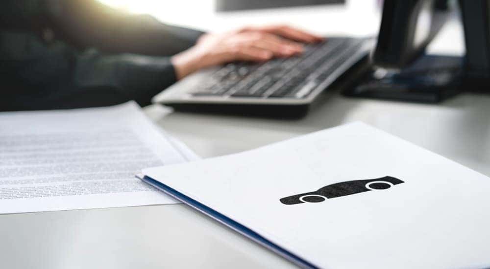 A salesman is shown typing on a keyboard next to car paperwork.