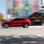 A red 2021 Ford Mustang Mach-E is shown from the side driving on a city street.