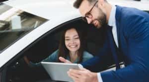 A salesman is shown speaking to a customer about a vehicle at a dealership.