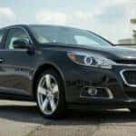 A black 2014 Chevy Malibu is shown from the front at an angle after leaving a used car dealership in Albany.