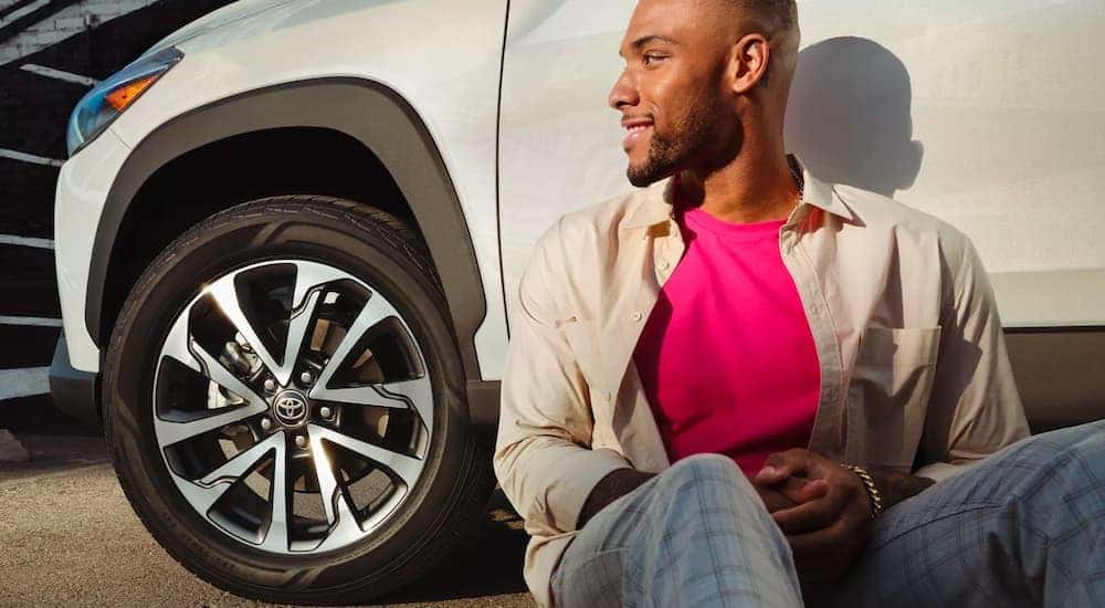 Man sitting against a parked white 2022 Toyota Corolla Cross XLE.