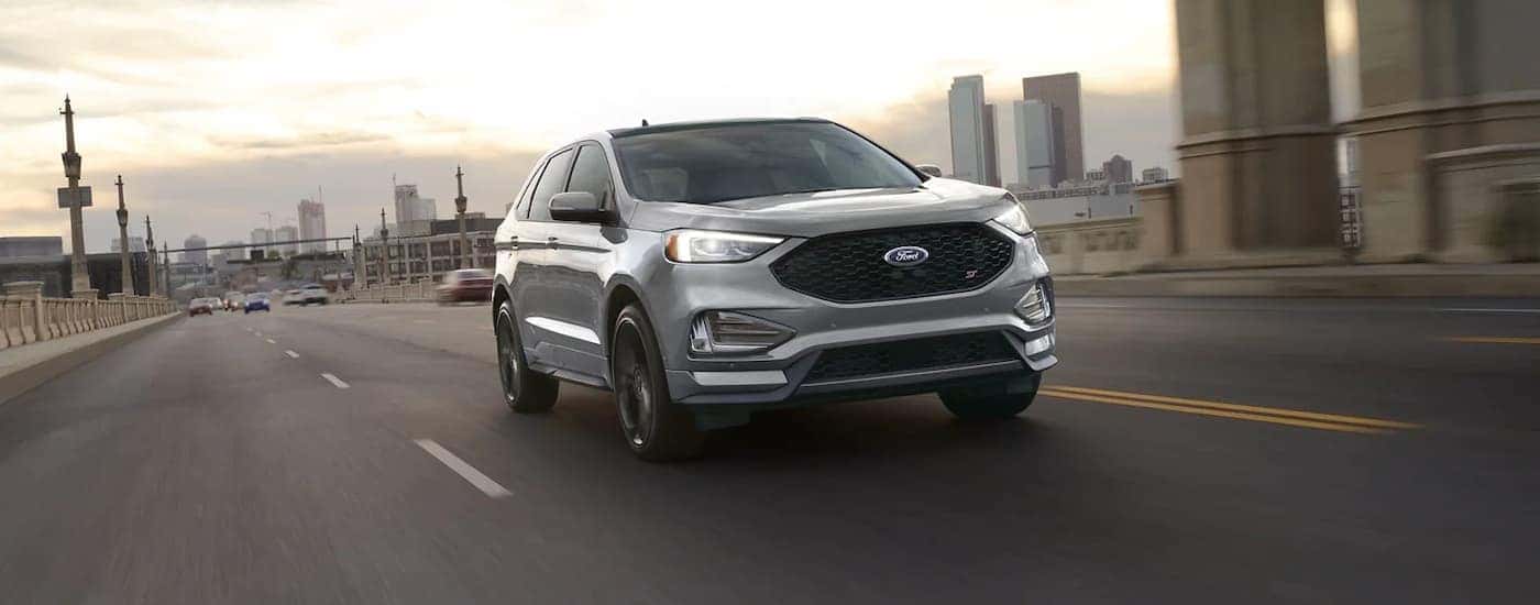 A grey 2023 Ford Edge ST is shown driving on a city highway after viewing used SUVs for sale.