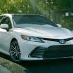 A white 2021 Toyota Camry is shown driving on a city street after viewing used cars for sale.