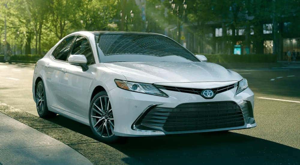 White 2021 Toyota Camry is shown driving on a city street after viewing used cars for sale.