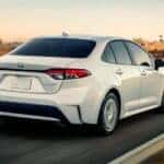 A white 2020 Toyota Corolla is shown driving from a rear angle after visiting with used cars for sale.