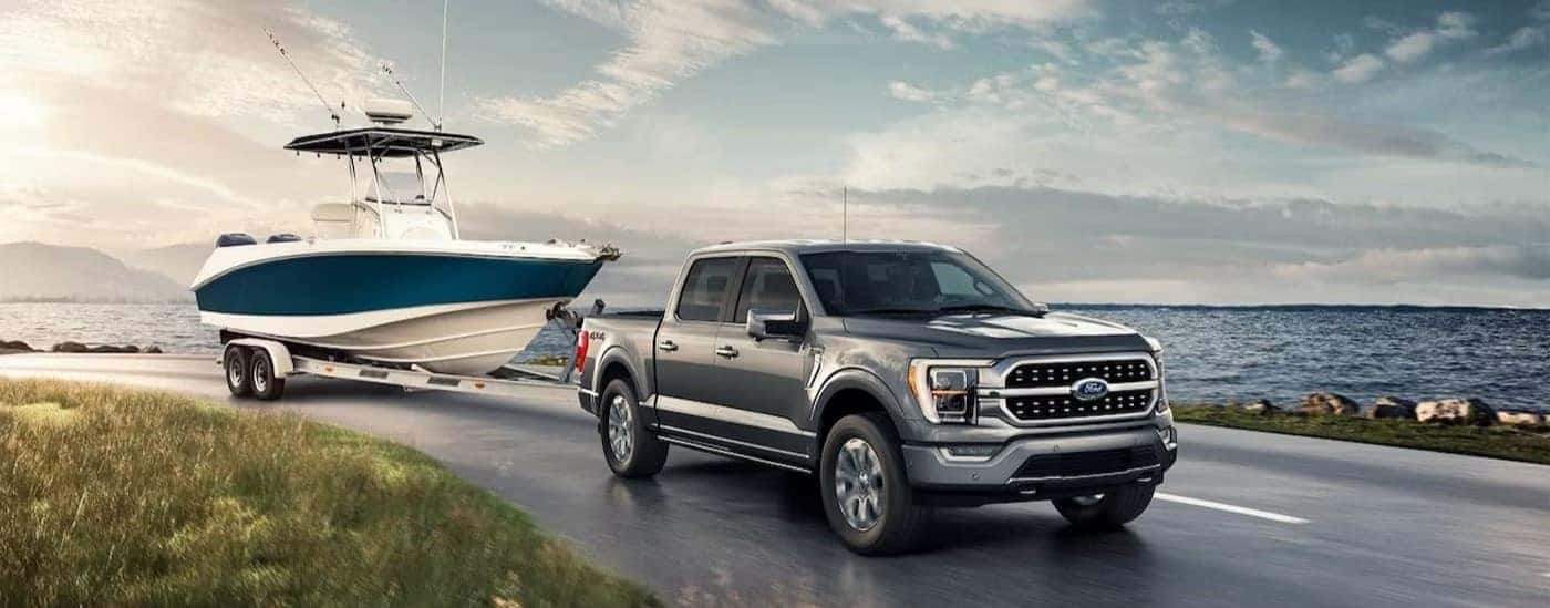 A gray 2023 Ford F-150 Lariat is shown towing a boat near water.