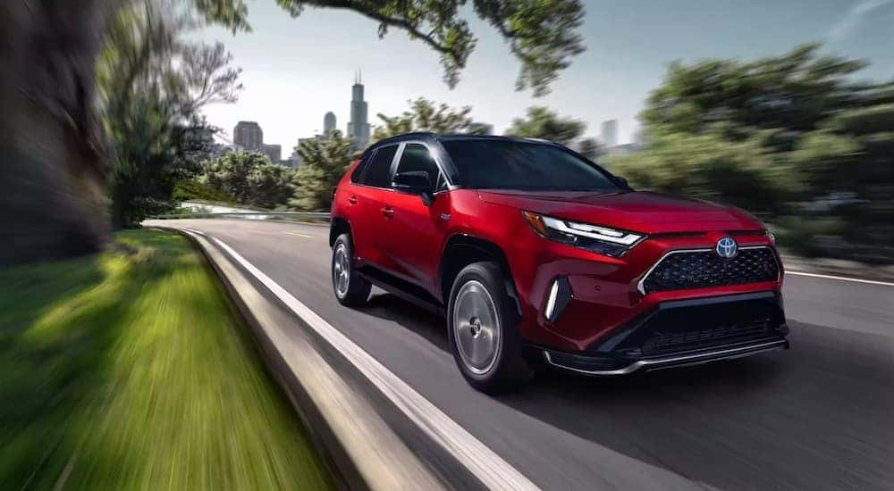 Red 2023 Toyota RAV4 Prime driving down a road.