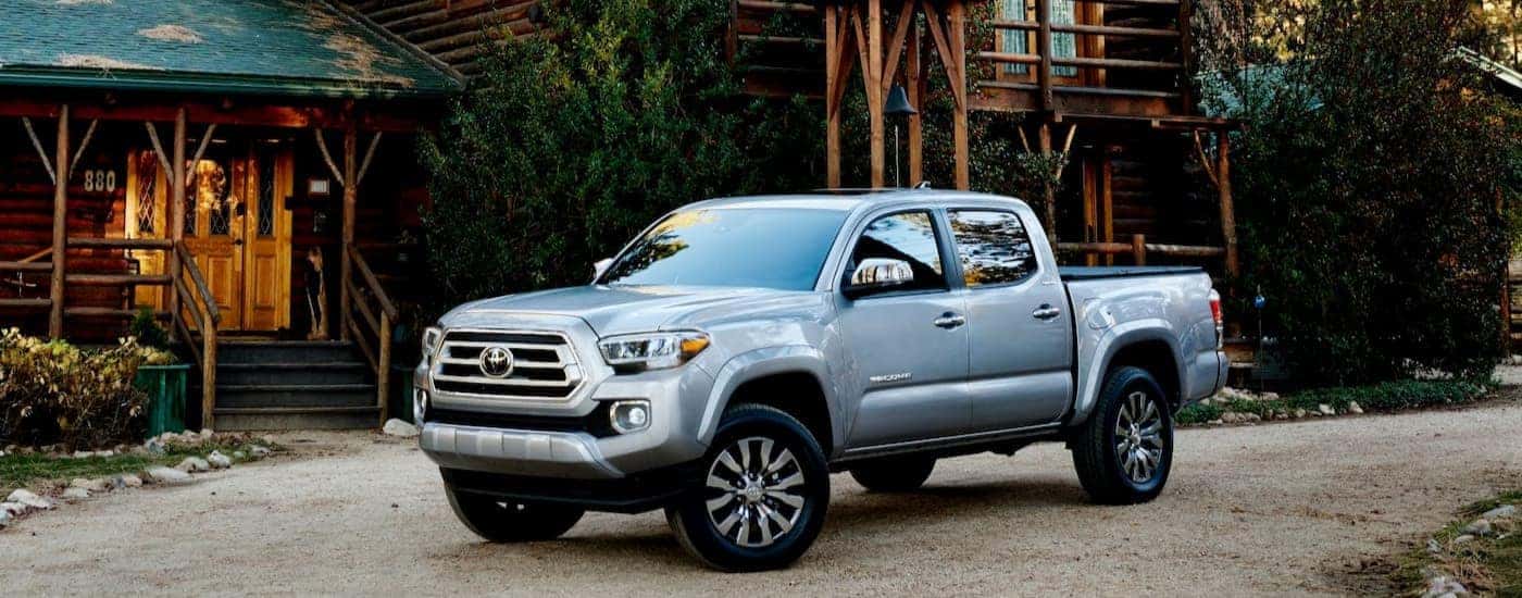 A silver 2023 Toyota Tacoma is shown parked near a log cabin.