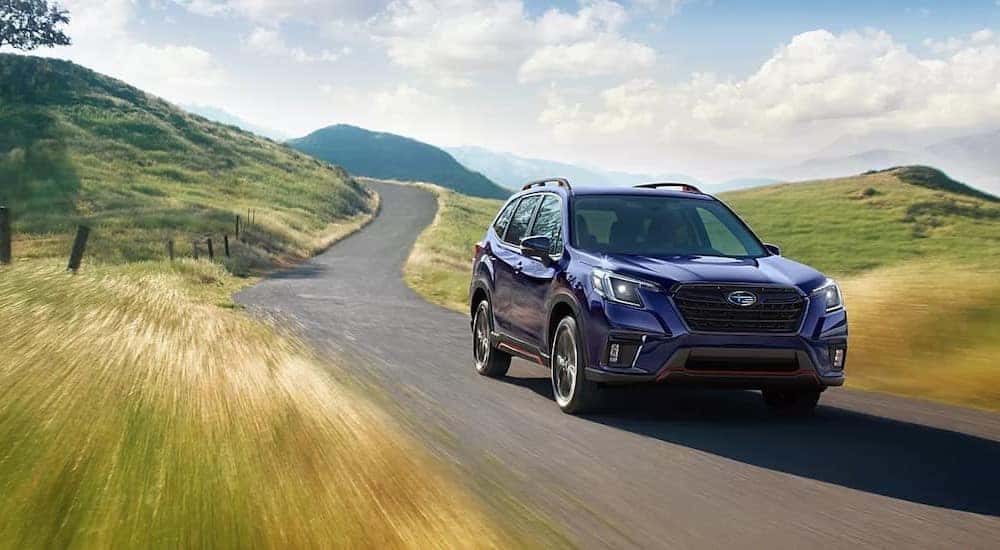 A purple 2023 Subaru Forester is shown driving on a country road.
