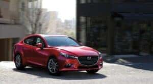 A red 2018 Mazda3 is shown driving to view used cars for sale near Troy.