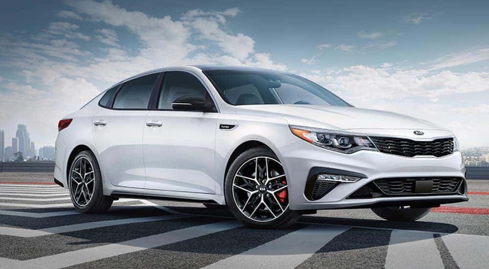 A white 2020 Kia Optima is shown parked near a city.