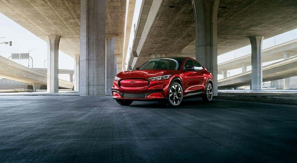 A red 2021 Ford Mustang Mach-E is shown parked under an overpass.